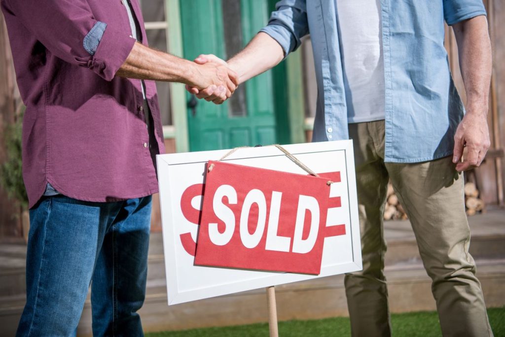 Real Estate Attorney Shaking Hands with Client Behind Sold Sign in Nassau County, NY